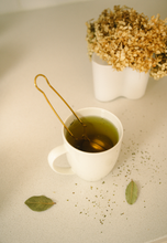 Load image into Gallery viewer, Gold tea strainer by Bamboo Switch in use, in white mug.
