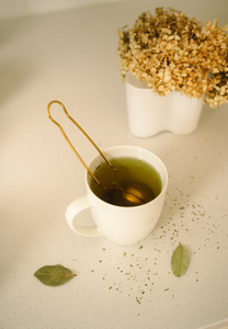 Gold tea strainer by Bamboo Switch in use, in white mug.