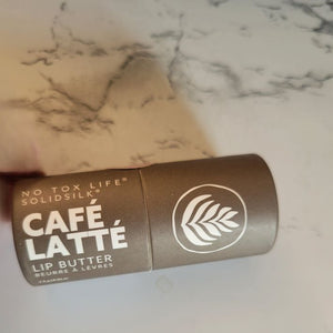 A brown paperboard tube of No Tox Life lip butter in "cafe latte" sits on a table. 