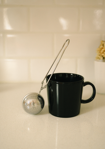 Reuseable stainless steel tea strainer by Bamboo Switch rests against a black coffee mug.