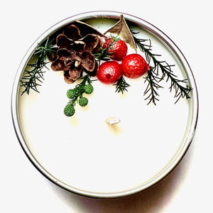 A winter walk candle in a tin, decorated with berries, pine, and pinecone. 