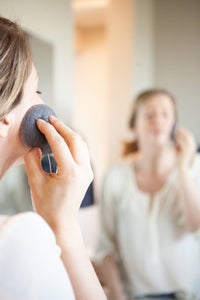 White woman using a charcoal infused Konjac sponge on her face.